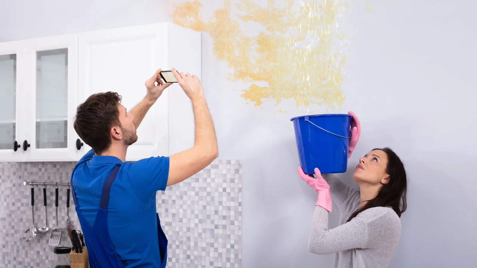 Homeowners photographing a water-stained wall while holding a bucket
