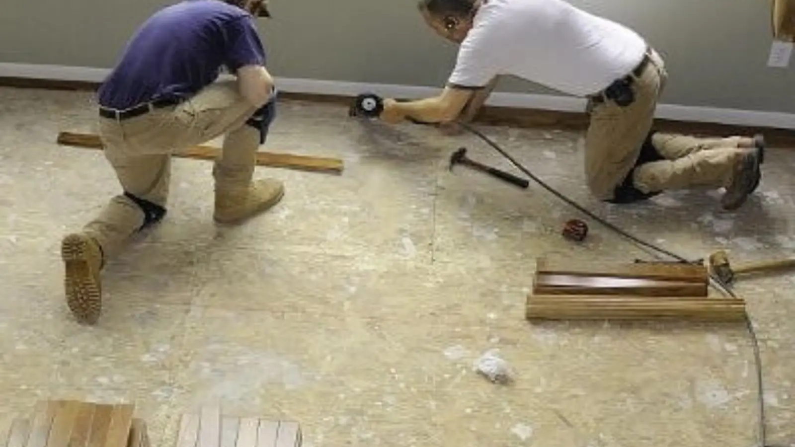 Two workers kneeling on a floor to repair the subfloor after water damage