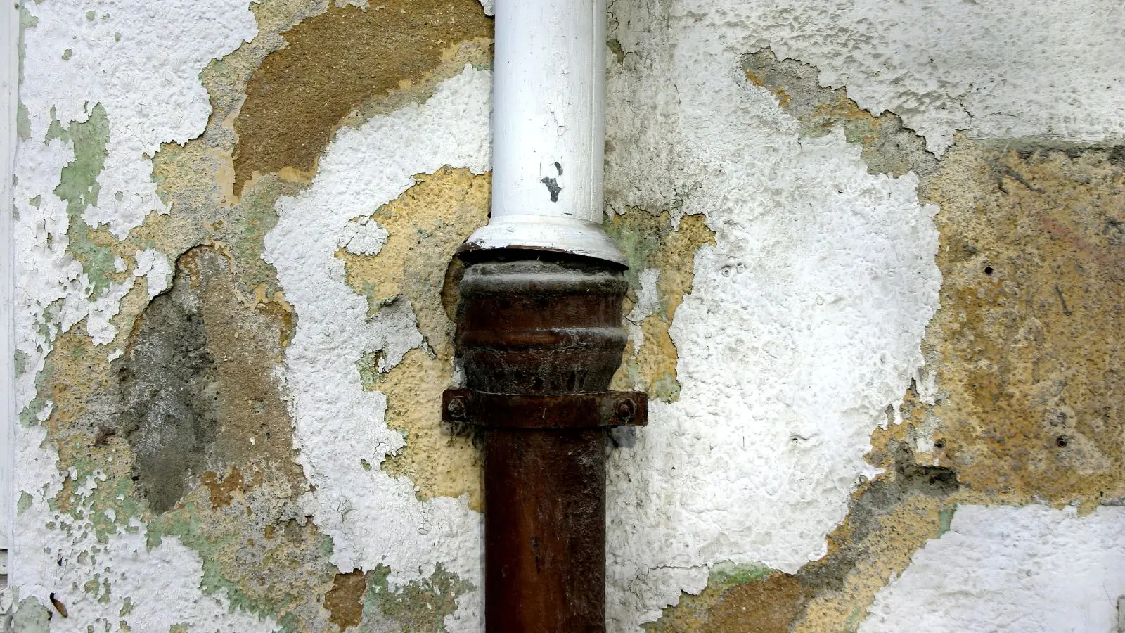 Peeling, stained wall paint around a rusted pipe, a common sign of water damage